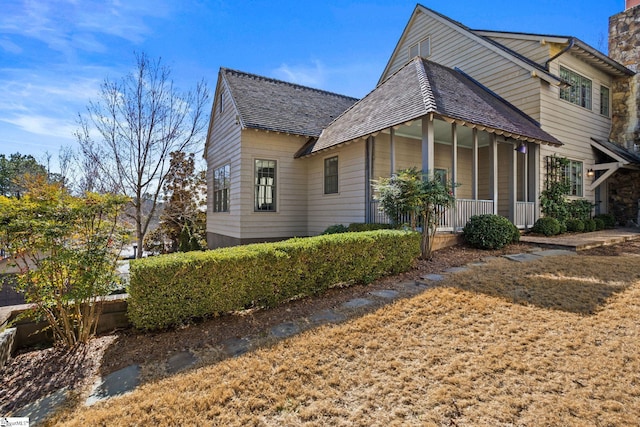 view of side of home with covered porch, a chimney, and a shingled roof