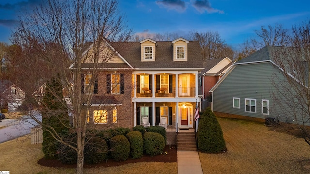 view of front of house with a balcony, central AC unit, a yard, covered porch, and a shingled roof