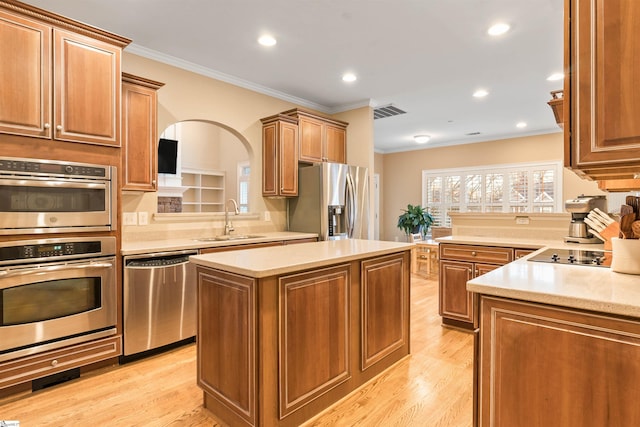 kitchen with a sink, light wood-type flooring, appliances with stainless steel finishes, and crown molding