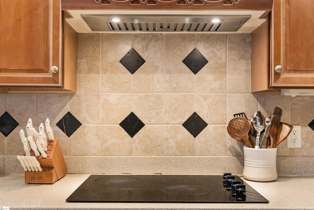 room details with brown cabinetry, premium range hood, decorative backsplash, light countertops, and black electric stovetop