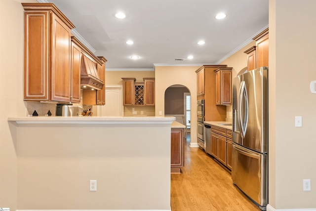 kitchen featuring light wood-style flooring, stainless steel appliances, arched walkways, a peninsula, and light countertops