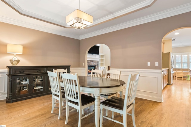 dining space featuring light wood-type flooring, arched walkways, a stone fireplace, and wainscoting