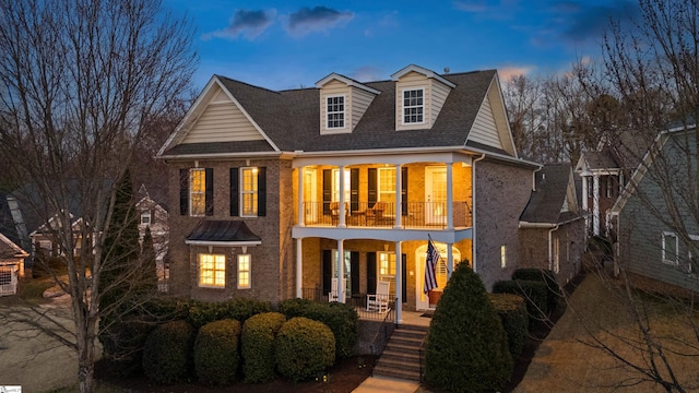 view of front of home featuring brick siding, a porch, a balcony, and a shingled roof