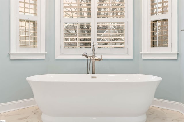 bathroom with baseboards, a freestanding bath, and marble finish floor