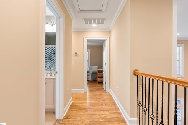 hall with visible vents, baseboards, ornamental molding, light wood-style flooring, and a sink