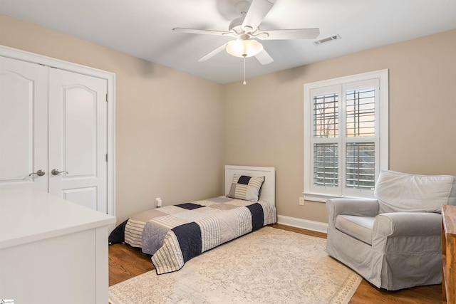 bedroom with a ceiling fan, wood finished floors, visible vents, and baseboards