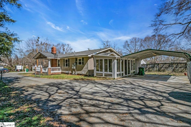 view of front of home featuring a detached carport, fence, driveway, a sunroom, and a chimney