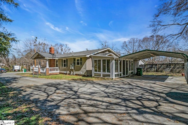 view of front facade with driveway, fence, a detached carport, a sunroom, and a chimney