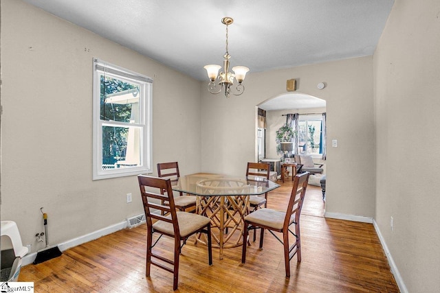 dining room with visible vents, baseboards, a chandelier, wood finished floors, and arched walkways