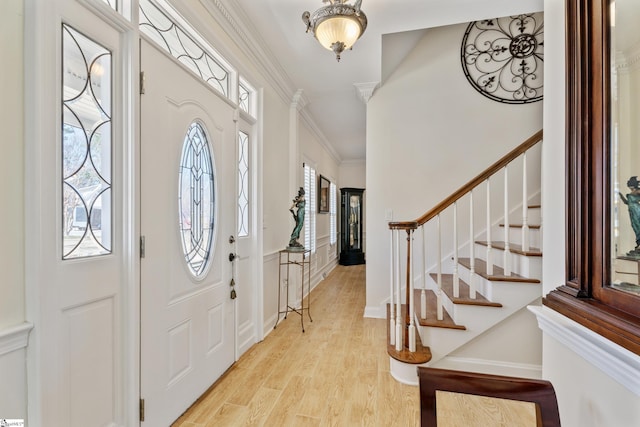 foyer entrance with stairs, light wood-style floors, baseboards, and ornamental molding