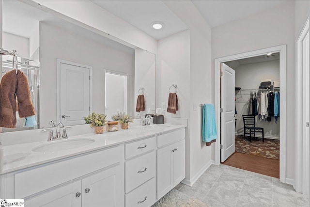 full bath with a sink, a walk in closet, baseboards, and double vanity