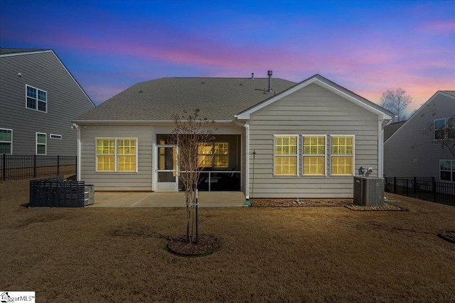 back of house at dusk with a patio area, central air condition unit, fence, and a lawn