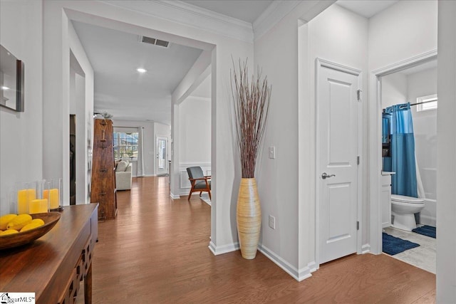 hallway with visible vents, baseboards, wood finished floors, and crown molding