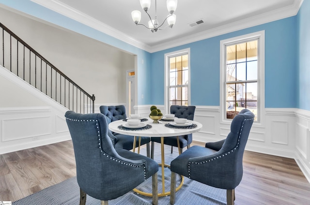 dining space featuring visible vents, wood finished floors, crown molding, a chandelier, and stairs