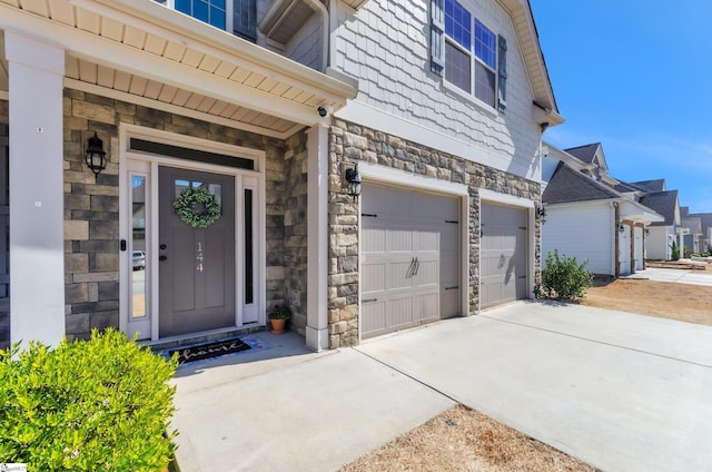 property entrance featuring an attached garage, stone siding, and driveway