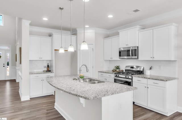 kitchen featuring crown molding, a center island with sink, appliances with stainless steel finishes, wood finished floors, and a sink