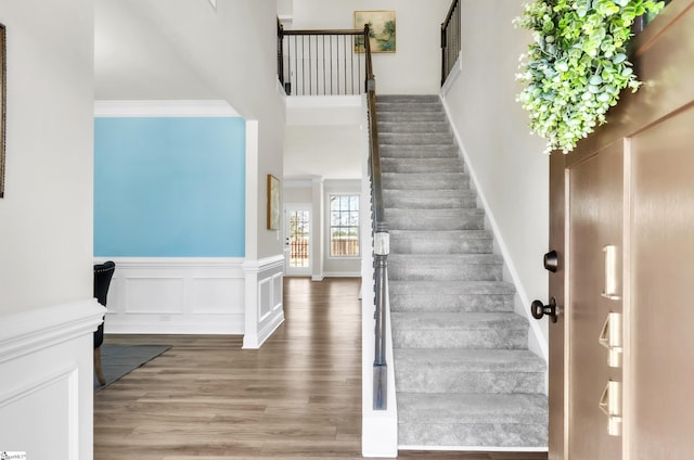 stairs with a wainscoted wall, ornamental molding, wood finished floors, a decorative wall, and a towering ceiling