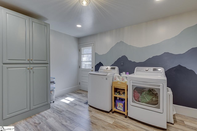 clothes washing area with light wood-type flooring, cabinet space, separate washer and dryer, and baseboards