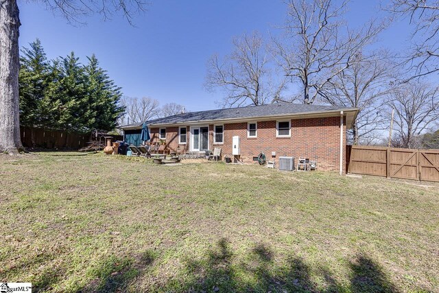 rear view of house featuring brick siding, central AC unit, a lawn, and fence