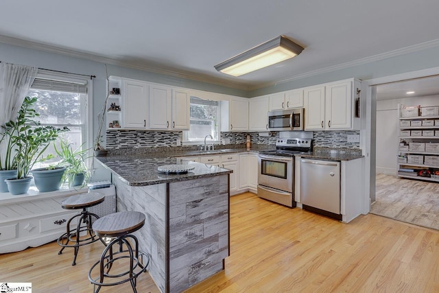 kitchen featuring appliances with stainless steel finishes, a peninsula, a kitchen breakfast bar, white cabinets, and a sink