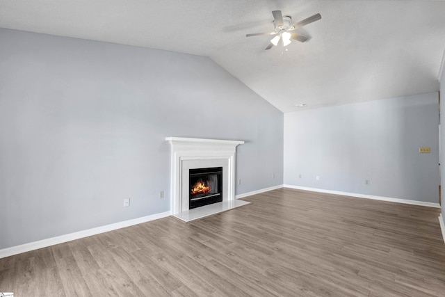 unfurnished living room with a ceiling fan, a warm lit fireplace, wood finished floors, baseboards, and vaulted ceiling