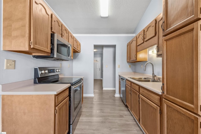 kitchen featuring light wood-style flooring, stainless steel appliances, light countertops, and a sink