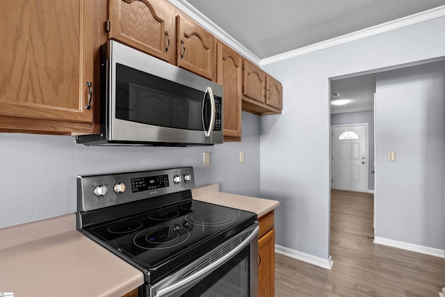 kitchen with baseboards, ornamental molding, stainless steel appliances, light countertops, and brown cabinets