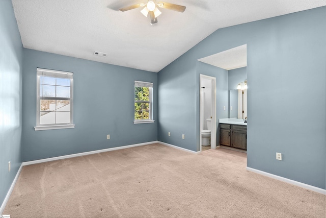 unfurnished bedroom featuring visible vents, ensuite bathroom, baseboards, light colored carpet, and vaulted ceiling