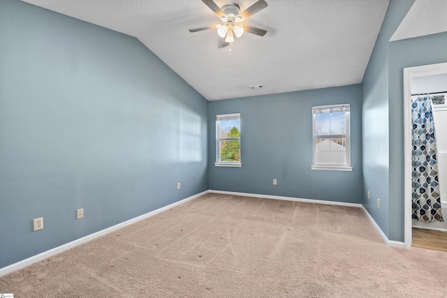 unfurnished room with carpet, baseboards, ceiling fan, vaulted ceiling, and a textured ceiling