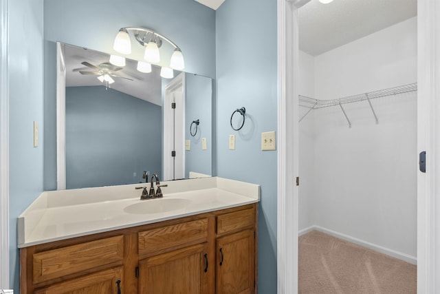 bathroom featuring baseboards, a spacious closet, ceiling fan, vanity, and vaulted ceiling