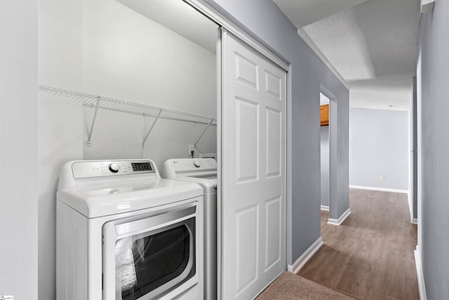 washroom featuring washing machine and clothes dryer, baseboards, laundry area, wood finished floors, and a textured ceiling