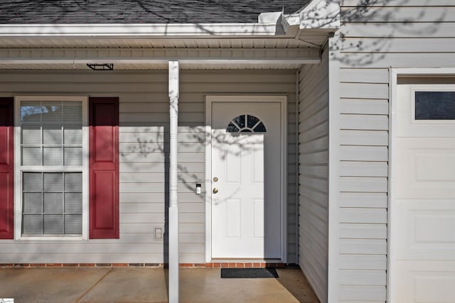 view of exterior entry featuring a garage and a shingled roof