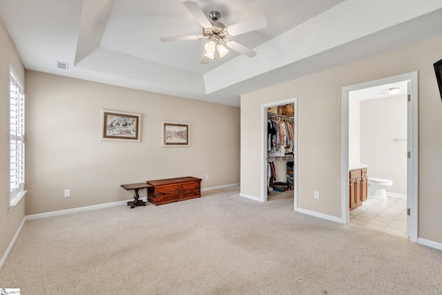 bedroom with visible vents, light carpet, a raised ceiling, a walk in closet, and baseboards