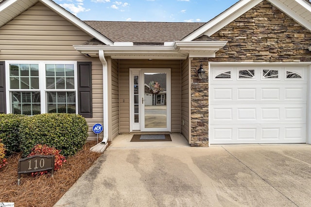 doorway to property with concrete driveway, an attached garage, stone siding, and roof with shingles