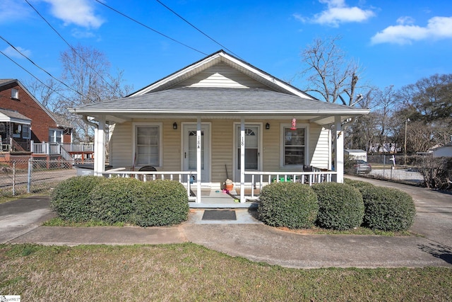 bungalow-style home featuring fence, covered porch, and roof with shingles