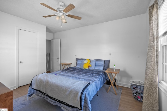 bedroom featuring ceiling fan, a textured ceiling, baseboards, and wood finished floors