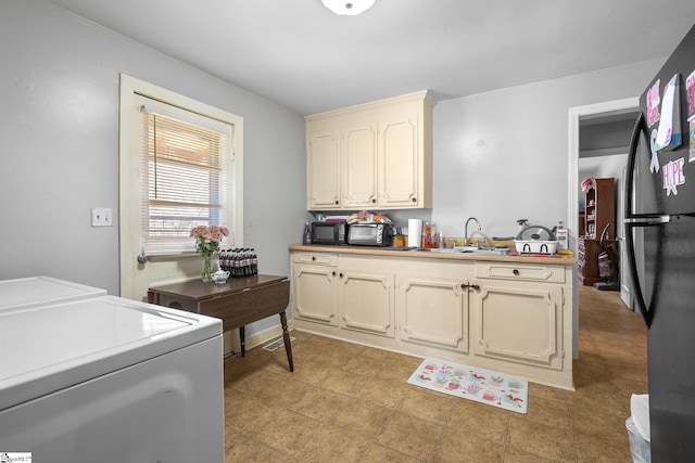 kitchen with a sink, cream cabinetry, washer and dryer, and freestanding refrigerator