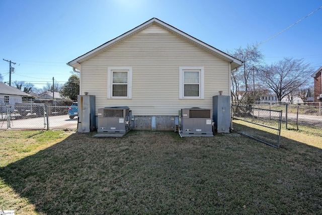 rear view of house with a lawn, cooling unit, fence, and a gate