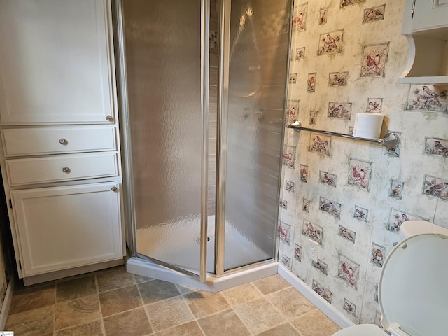 full bathroom featuring toilet, stone finish flooring, a shower stall, wallpapered walls, and baseboards