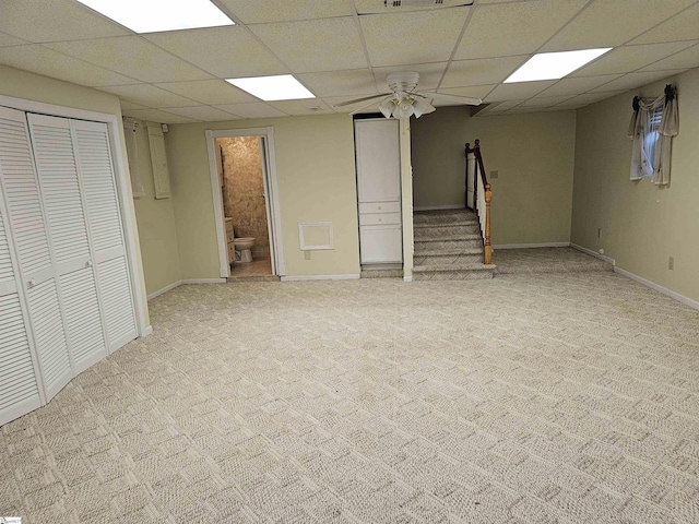 finished below grade area featuring light carpet, stairway, baseboards, and a drop ceiling