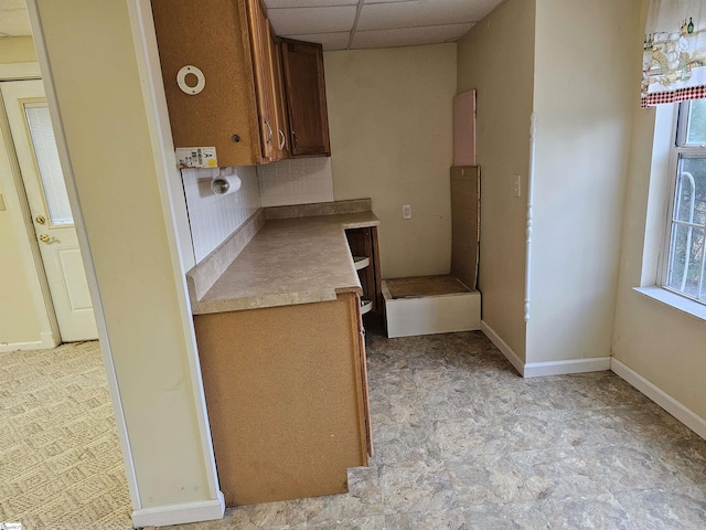 kitchen featuring tasteful backsplash, light countertops, a paneled ceiling, and baseboards