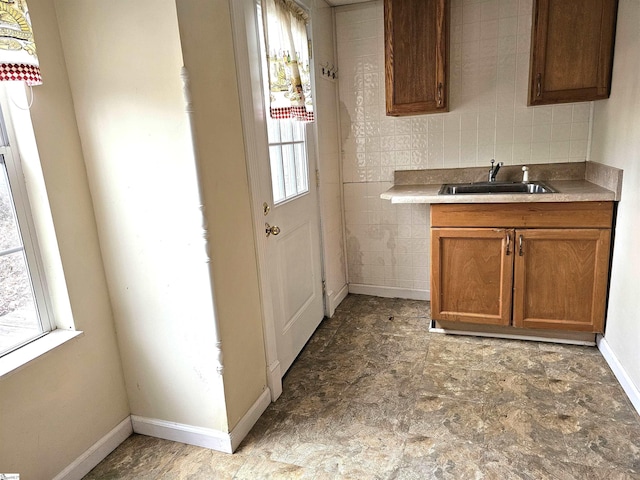 kitchen with brown cabinetry, baseboards, a sink, decorative backsplash, and light countertops