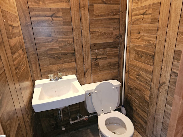 bathroom with toilet, wood walls, and a sink