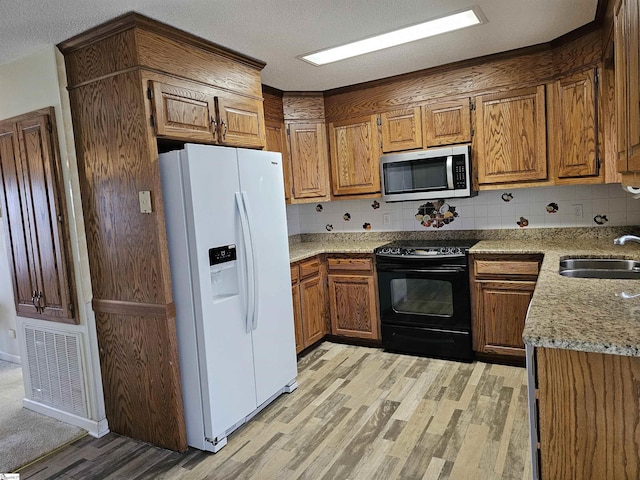 kitchen with black / electric stove, visible vents, a sink, white refrigerator with ice dispenser, and stainless steel microwave