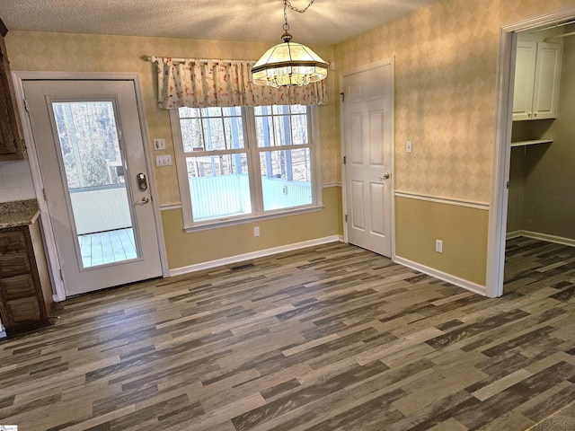 unfurnished dining area featuring wallpapered walls, baseboards, dark wood-style flooring, and a textured ceiling