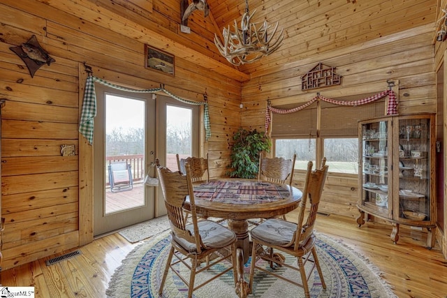 dining area featuring wooden walls, visible vents, light wood finished floors, high vaulted ceiling, and french doors