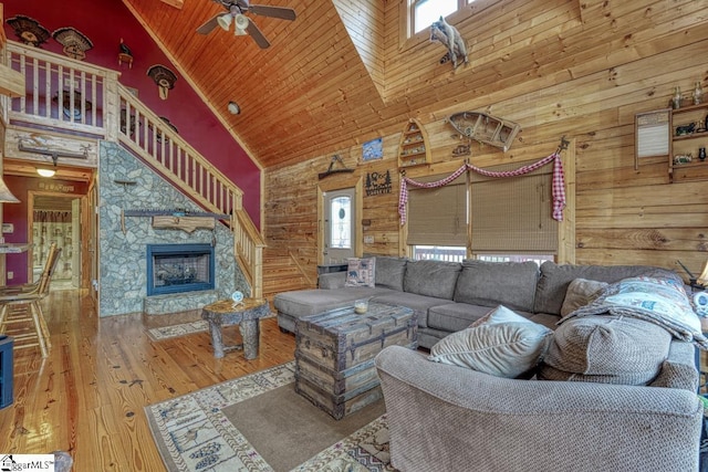 living room with high vaulted ceiling, wood finished floors, wooden walls, a stone fireplace, and wooden ceiling