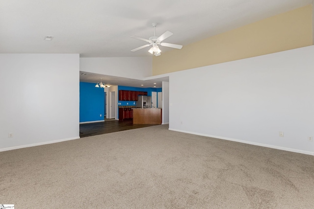 unfurnished living room with ceiling fan with notable chandelier, baseboards, dark carpet, and high vaulted ceiling