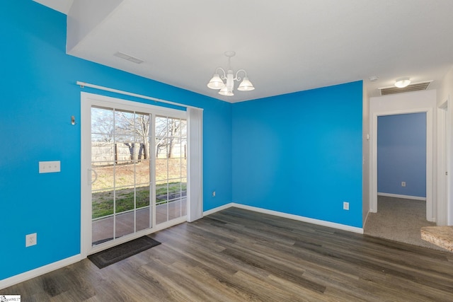 empty room with visible vents, an inviting chandelier, baseboards, and wood finished floors