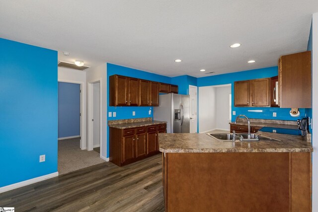 kitchen featuring stainless steel refrigerator with ice dispenser, a sink, dark wood-style floors, a peninsula, and baseboards